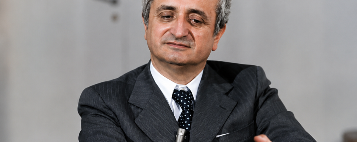 Ritratto storico di Vittorino Colombo durante un'intervista, seduto al tavolo con microfono, in un momento della sua attività politica e istituzionale.