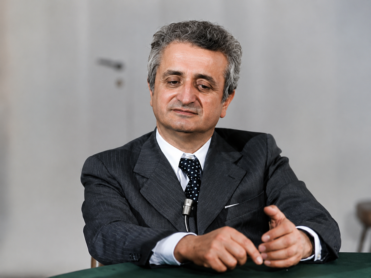 Ritratto storico di Vittorino Colombo durante un'intervista, seduto al tavolo con microfono, in un momento della sua attività politica e istituzionale.